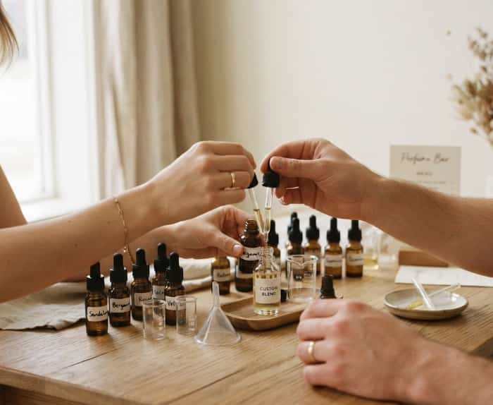 Couple blending custom fragrance oils at wooden table in cozy studio