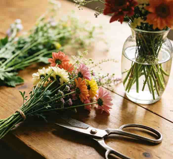 Fresh local flowers and scissors on a table next to a half-arranged vase in natural light