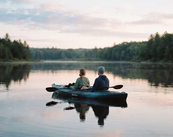 A young couple paddling a tandem kayak together on a calm lake during a misty sunrise