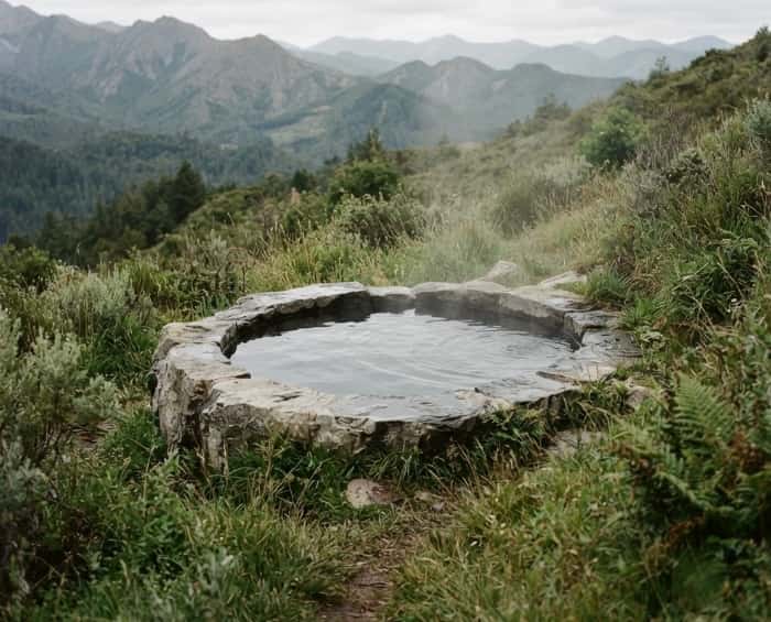 Minimalist stone hot spring pool on hillside with mountain view and soft steam