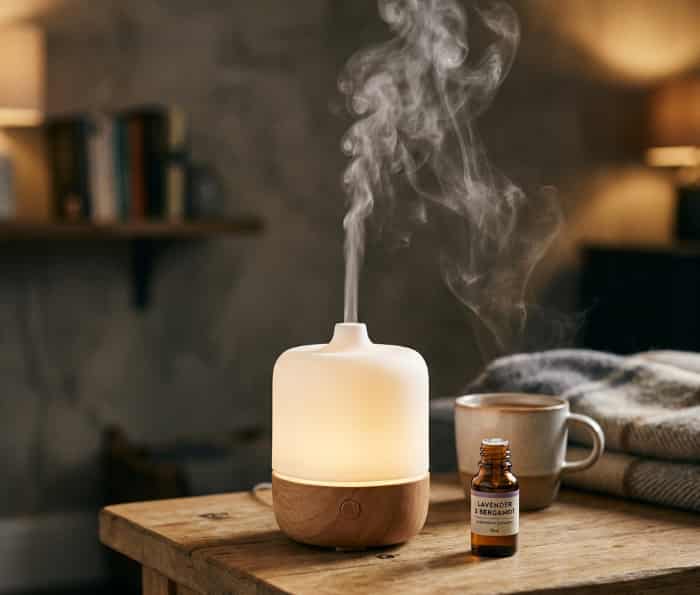 Ultrasonic aroma diffuser with warm light and mist on wooden side table