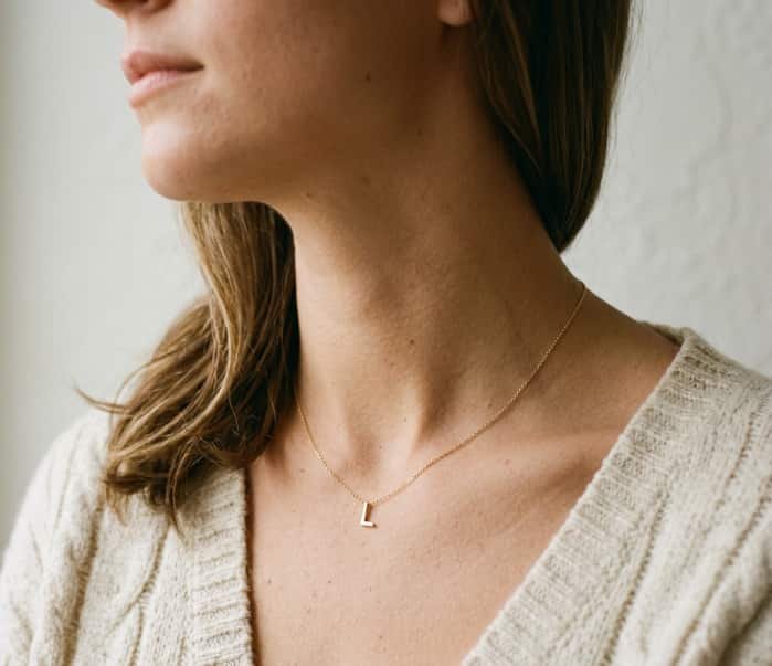 Woman wearing subtle gold initial pendant necklace with cozy knit sweater