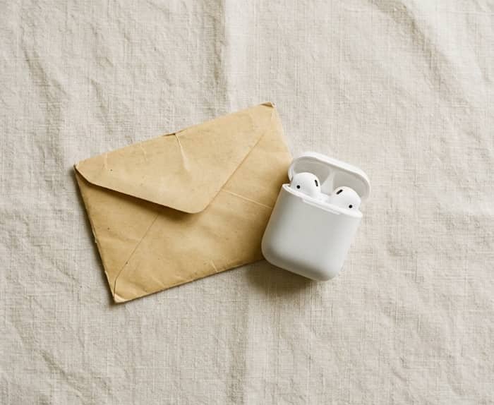 Open wireless earbud case next to kraft envelope on linen cloth