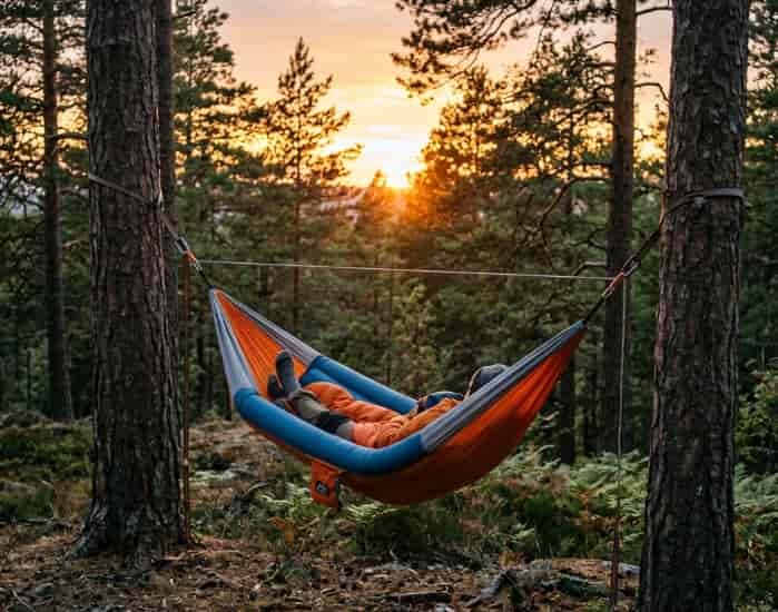 Inflatable camping hammock hung between two pine trees at sunset