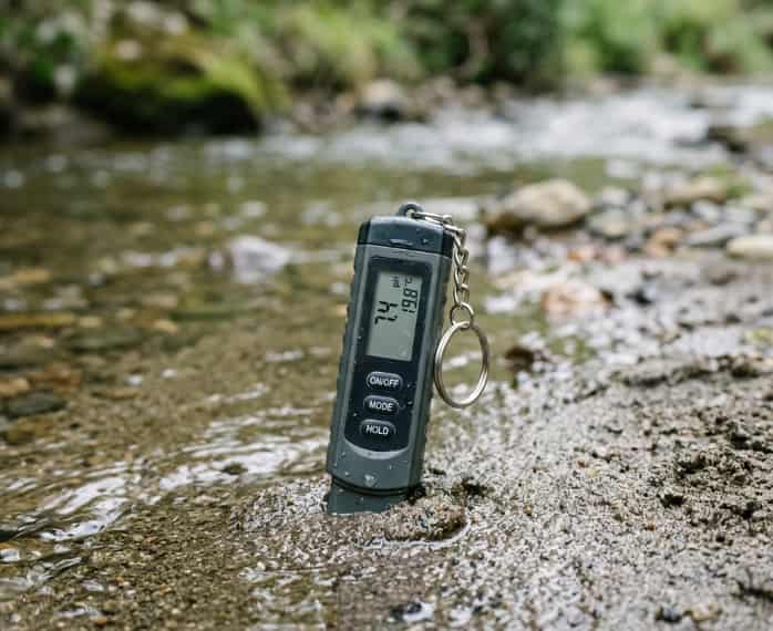 Keychain water quality tester stuck in wet sand by a creek