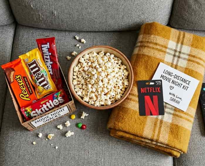 Overhead view of a movie night kit on a couch, with popcorn, candy, a blanket, and a streaming gift card