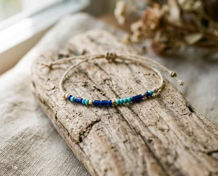 A delicate Morse code bracelet with blue and turquoise beads on a rustic driftwood background
