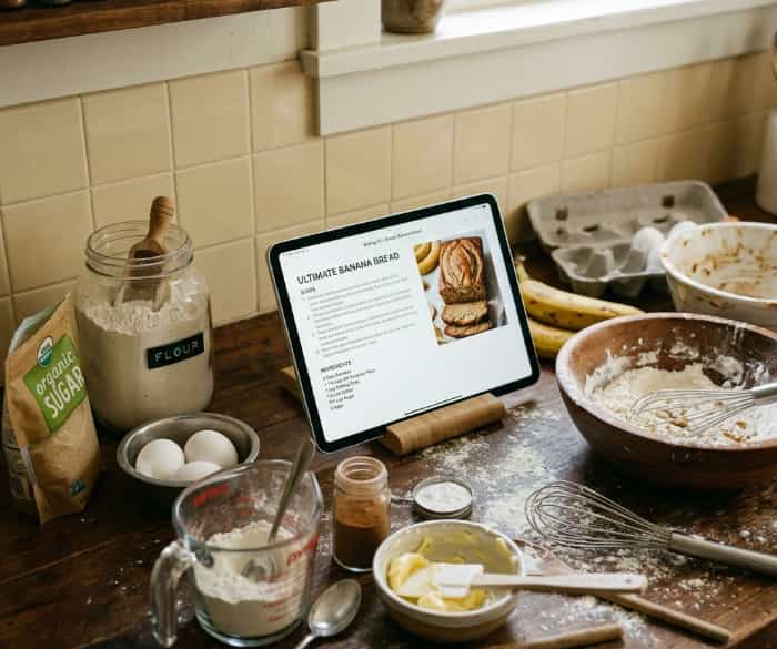 Tablet with a digital recipe surrounded by baking ingredients on a wooden kitchen counter