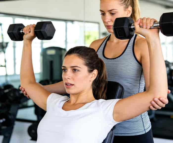 Personal trainer guiding client with dumbbells
