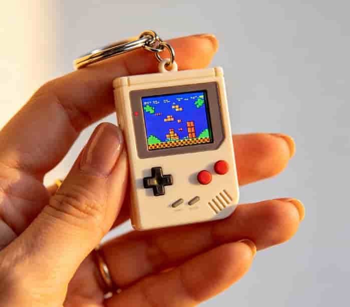 Tiny playable retro arcade keychain held between fingers with the screen turned on
