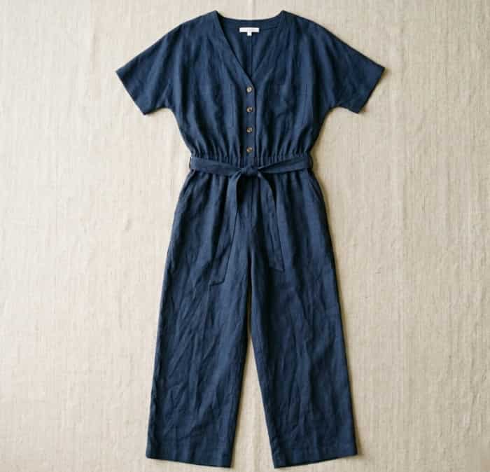 Navy linen jumpsuit laid flat on textured beige surface with soft natural light