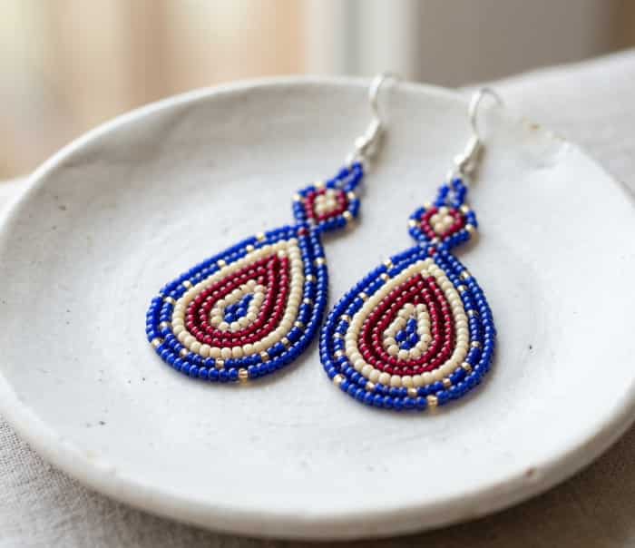 Hand-strung beaded teardrop earrings in ruby, ivory, and cobalt blue on white ceramic dish