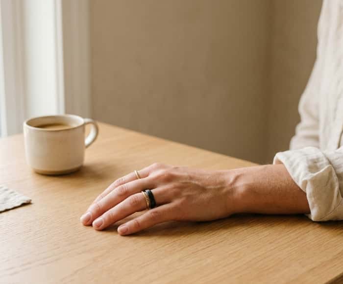 Woman wearing an AI smart wellness ring resting hand on wooden table