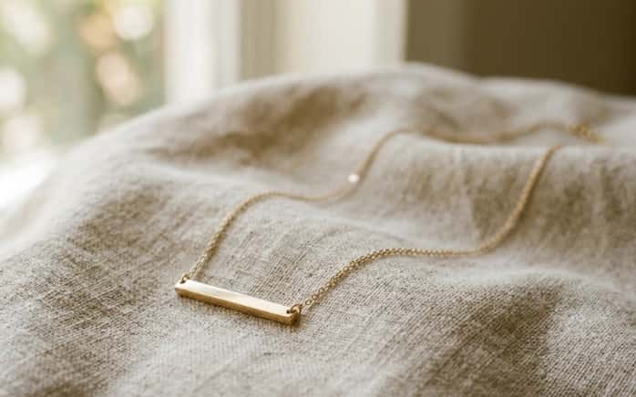 Gold bar necklace laid on textured linen fabric