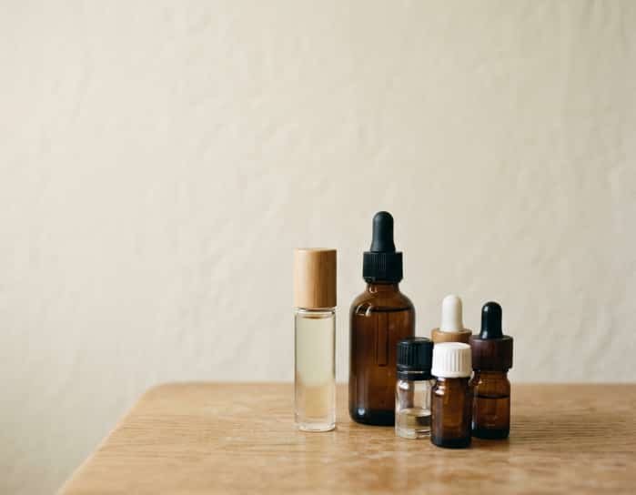 Small glass roller bottles and essential oil droppers arranged on a wooden board