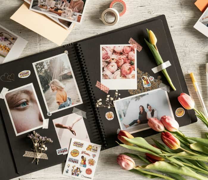 Decorated handmade scrapbook album with photos, stickers and tulips on wooden table