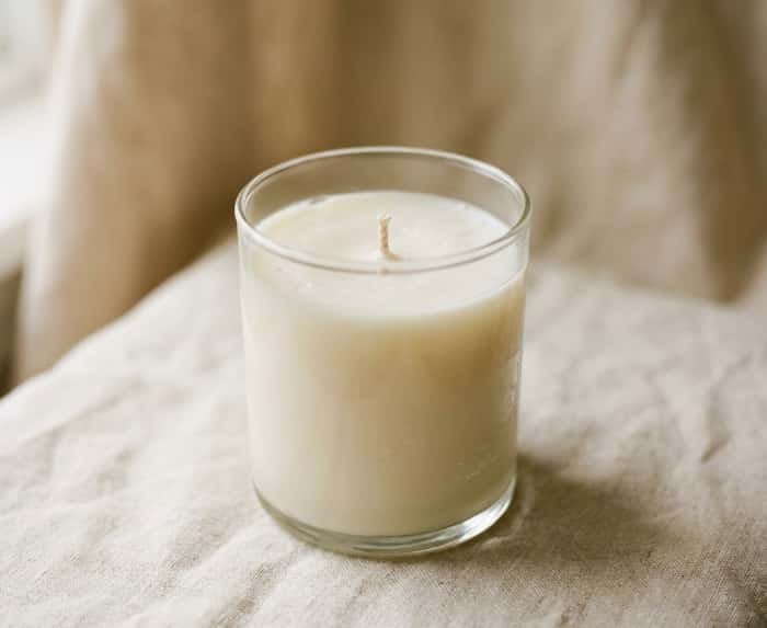Unlit soy wax candle in clear glass jar resting on linen fabric